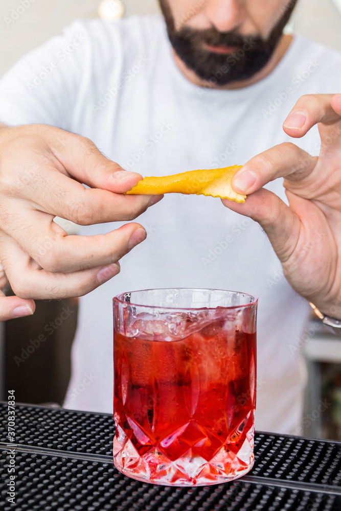 Faceless bearded barkeeper garnishing old fashioned cocktail in crystal glass with aromatic orange peel Faceless bearded barkeeper garnishing old fashioned cocktail in crystal glass with aromatic orange peel