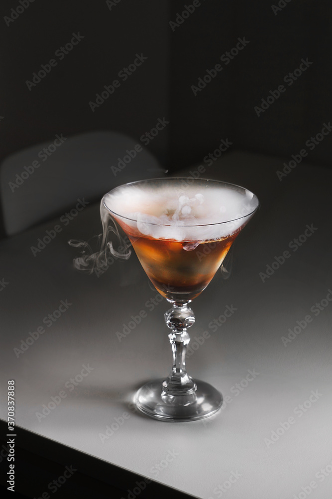 Elegant cocktail glass with brown alcoholic drink and smoking dry ice on gray table Elegant cocktail glass with brown alcoholic drink and smoking dry ice on gray table