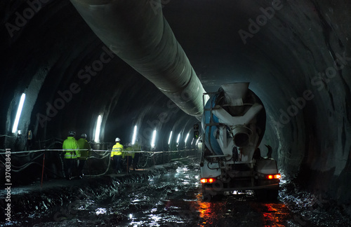Back view of company of employees in uniform walking along dirty underground passage near 	concrete mixer truck