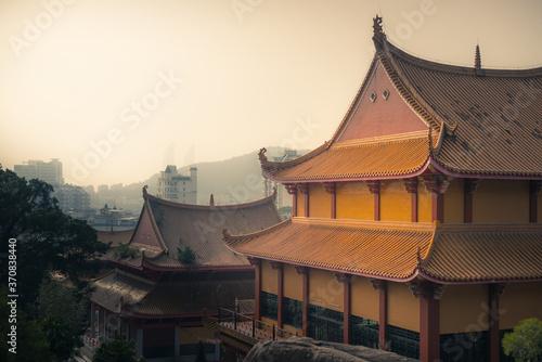 Exterior of traditional colorful oriental temple with ornamental roof located among green trees against gray cloudy sky in Xiamen in China
