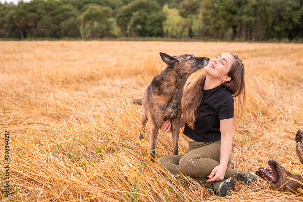 Female with closed eyes cuddling gently purebred dog with smooth coat while sitting in field with faded grass near forest in countryside under sky with clouds Female with closed eyes cuddling gently purebred dog with smooth coat while sitting in field with faded grass near forest in countryside under sky with clouds