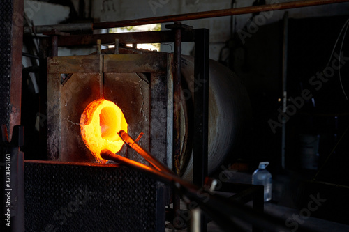 Blowpipe and melting glass in hot furnace in workshop