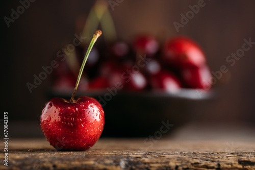 Close up view of cherry, on the background bowl full of fresh cherries on wooden table against dark background photo