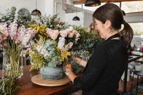 Side view of happy female designer arranging decorative blooming bouquets while working on order for event in creative floristry studio photo