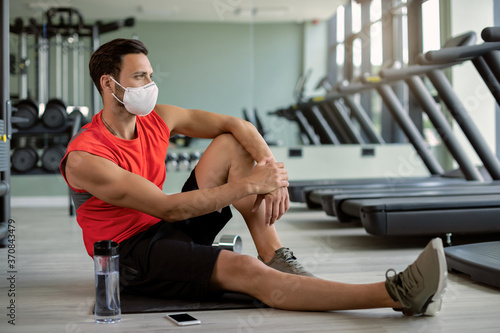 Pensive sportsman with protective face mask relaxing on the floor at health club.