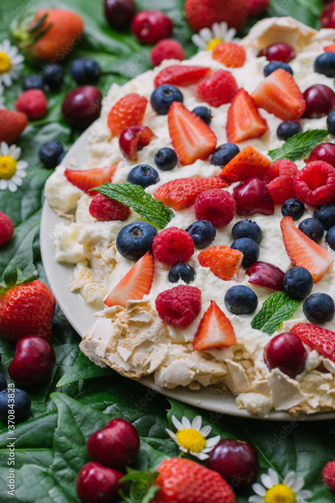 Plate with delicious summer dessert Pavlova cake with meringue and assorted fresh berries garnished with green leaves