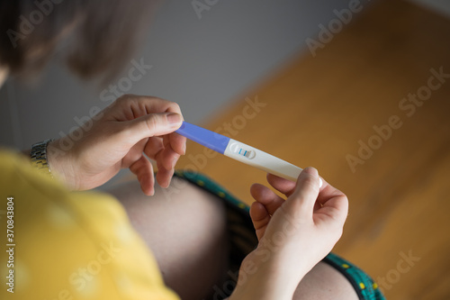 From above of crop female with underwear pulled down holding pregnancy test with double bars sitting in bathroom