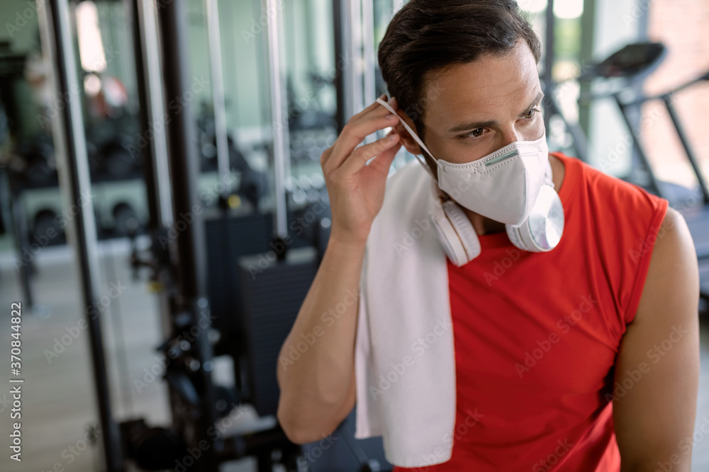 Athletic man putting on protective face mask in a gym.