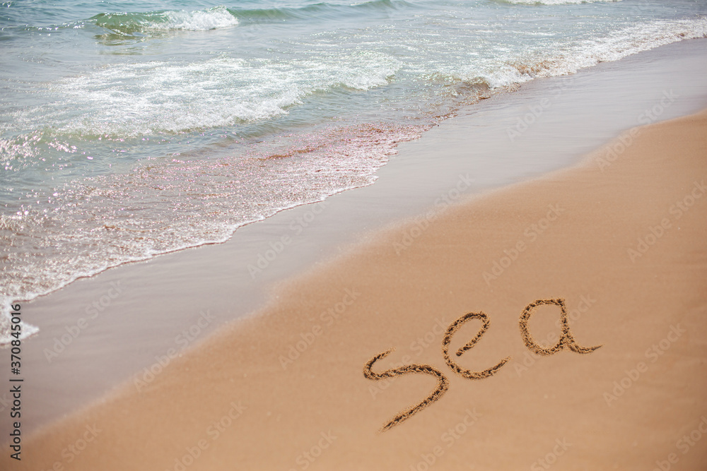 Fototapeta premium The inscription on the seashore is the word Sea. The foam wave is coming to the shore. The beautiful seascape.