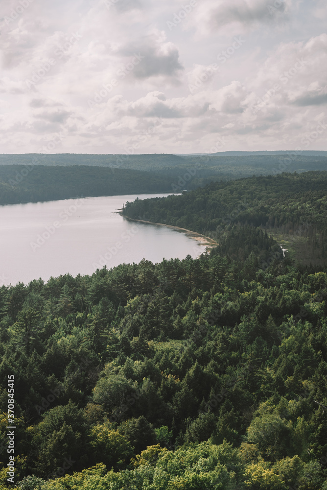 From above aerial view of calm lake surrounded by green trees and bushes under gray cloudy sky in late summer in Algonquin Provincial Park in Canada From above aerial view of calm lake surrounded by green trees and bushes under gray cloudy sky in late summer in Algonquin Provincial Park in Canada