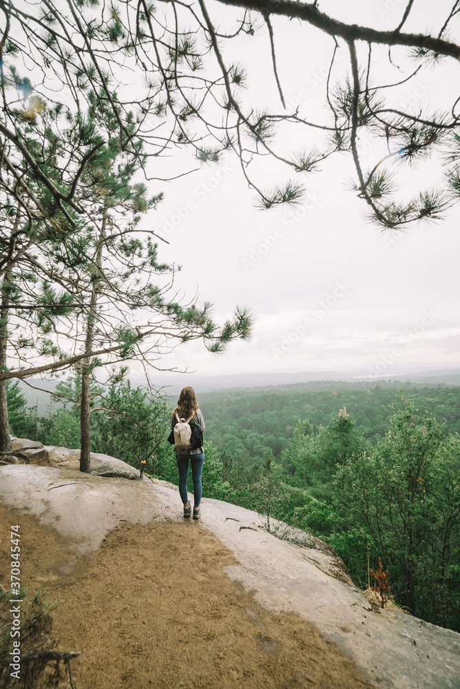 Full length back view of unrecognizable female backpacker walking on rocky mountain slope against green forest in cloudy day in Algonquin Provincial Park in Canada Full length back view of unrecognizable female backpacker walking on rocky mountain slope against green forest in cloudy day in Algonquin Provincial Park in Canada