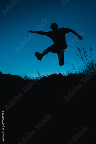Silhouette of a runner jumping down a hill under the moonlight