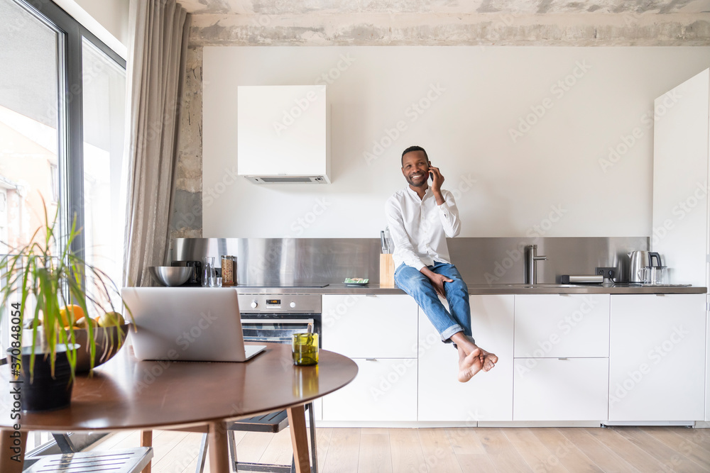 Portrait of smiling man on the phone sitting on kitchen counter in modern apartment Portrait of smiling man on the phone sitting on kitchen counter in modern apartment