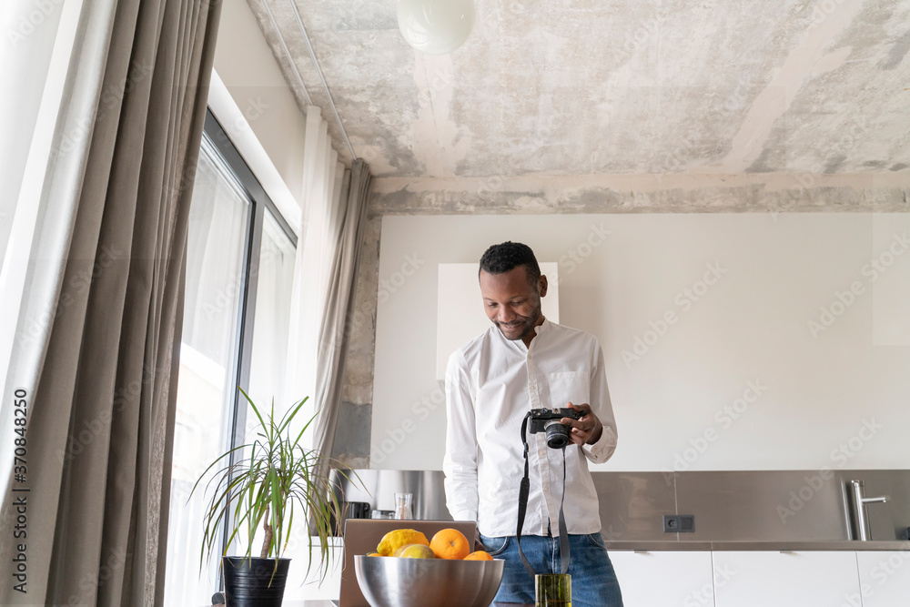 Smiling man using laptop and camera at home Smiling man using laptop and camera at home