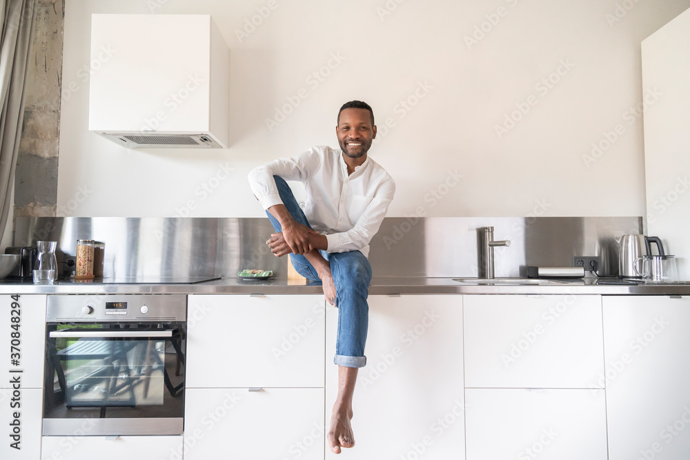 Portrait of smiling man sitting barefoot on kitchen counter at home Portrait of smiling man sitting barefoot on kitchen counter at home
