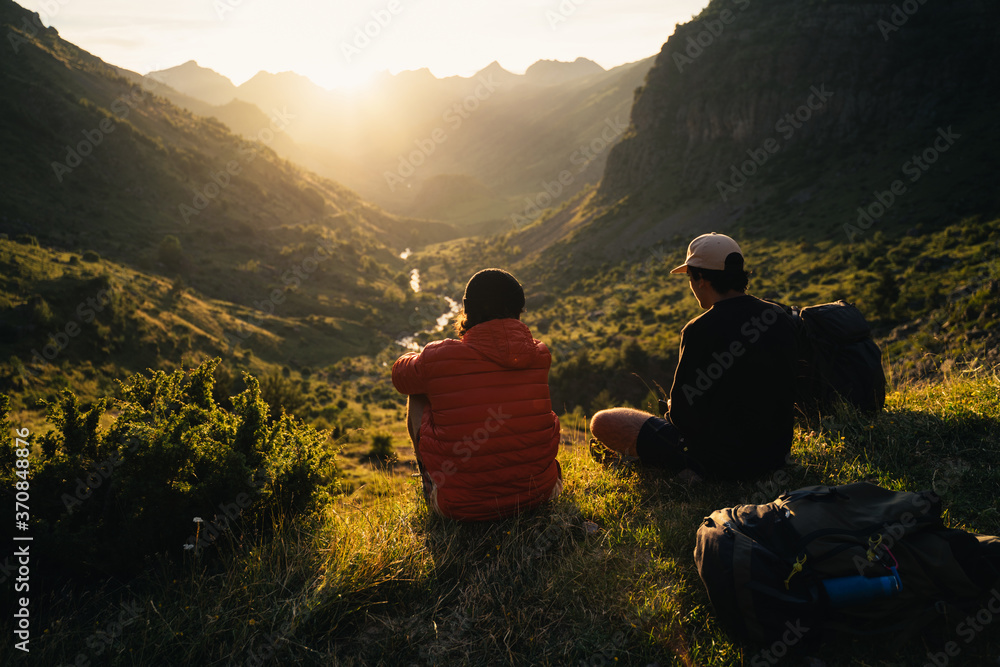 Two young men sitting on the grass watching the sunset on top of a valley in Pyrenees