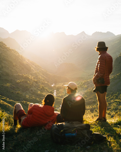 Group of young men sitting on the grass watching the sunset on top of a valley in Pyrenees