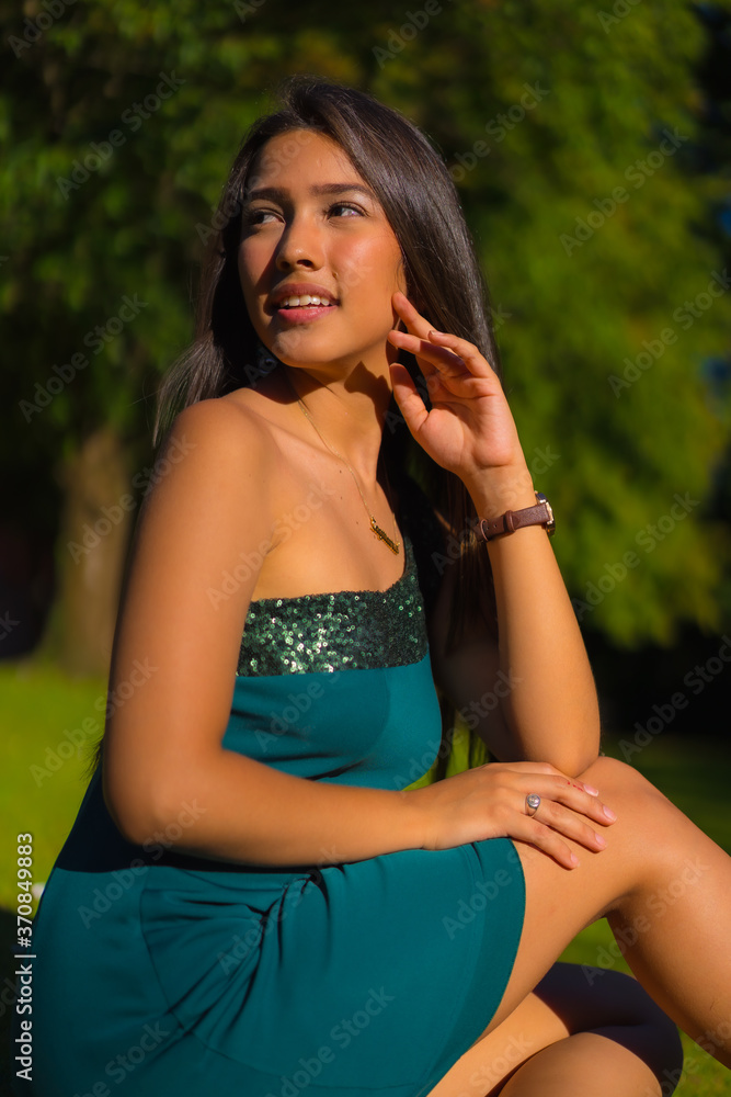 A pretty young brunette Latina with long straight hair, wearing a tight green dress. Portrait of a young girl dreaming and imagining things in a park with trees in summer A pretty young brunette Latina with long straight hair, wearing a tight green dress. Portrait of a young girl dreaming and imagining things in a park with trees in summer