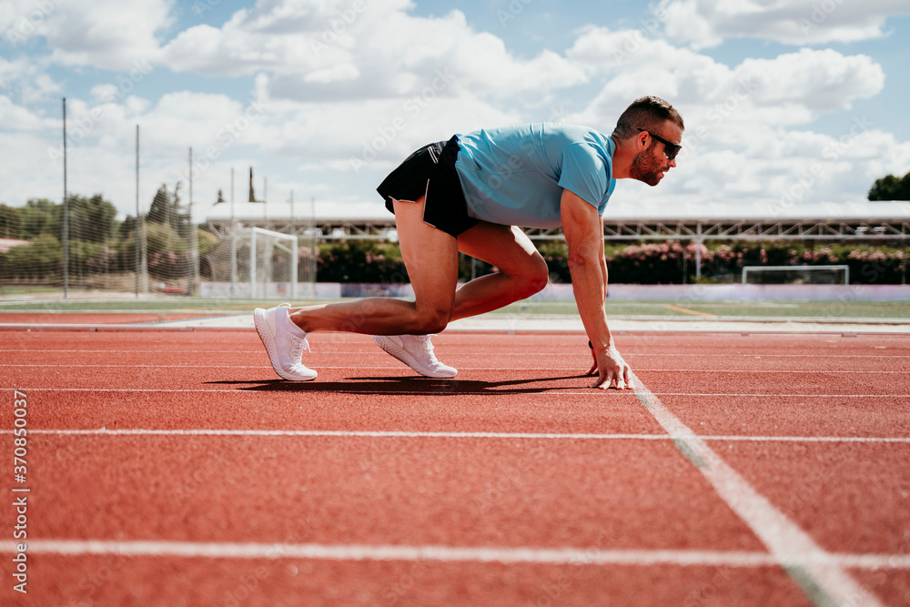Male athlete in starting position on tartan track Male athlete in starting position on tartan track