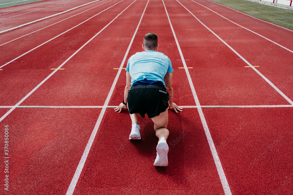 Male athlete in starting position on tartan track Male athlete in starting position on tartan track