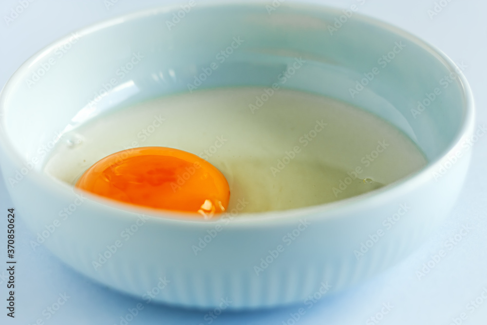 Fresh organic raw yolk and white of egg in light blue bowl on pastel background. Healthy breakfast and fresh ingredients. Selective focus
