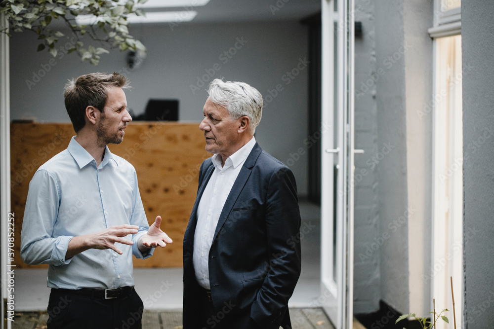Two businessmaen standing in open office door, talking Two businessmaen standing in open office door, talking