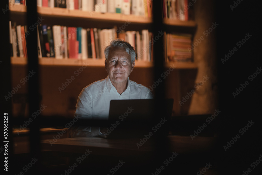 Senior businessman sitting in office, working late, smiling Senior businessman sitting in office, working late, smiling