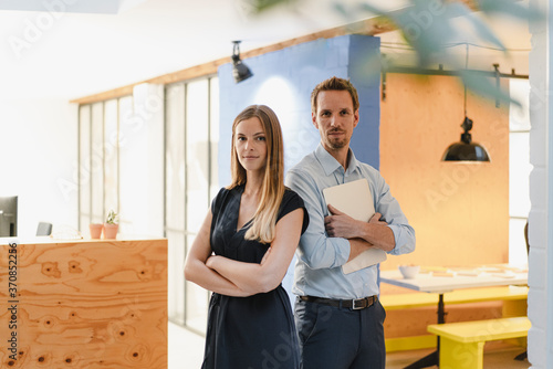 Businessman and businesswoman standing in modern office with arms crossed photo