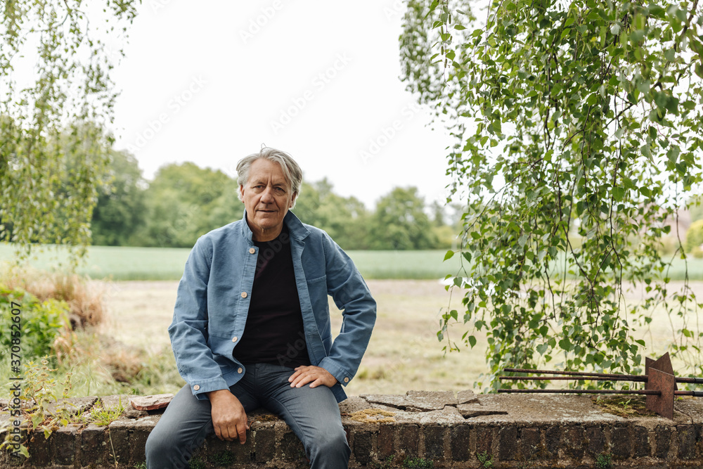 Senior man sitting on a brick wall in the countryside