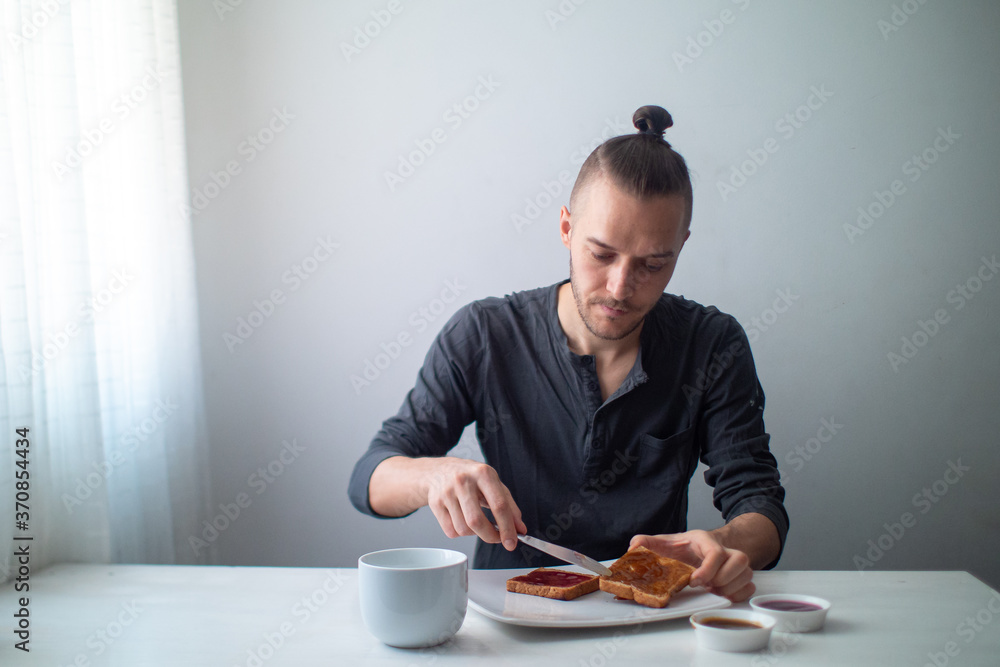 Blond Caucasian Man Preparing Toast with Fruit Jam on a White Table Blond Caucasian Man Preparing Toast with Fruit Jam on a White Table