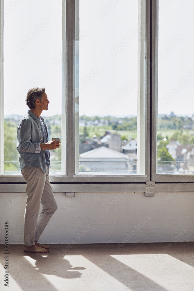Senior man looking out of window in a loft flat Senior man looking out of window in a loft flat