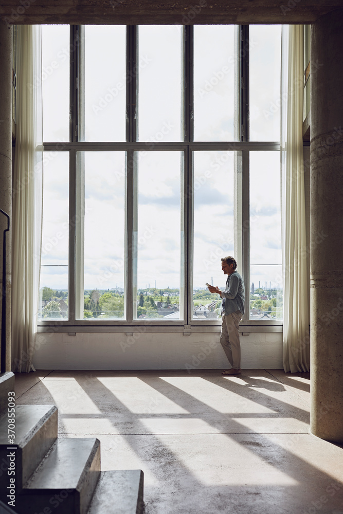 Senior man using smartphone at the window in a loft flat