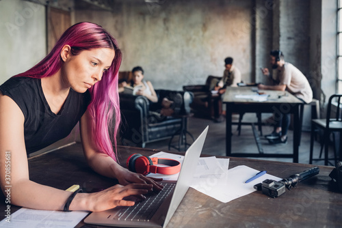 Creative businesswoman with pink hair using laptop in loft office photo