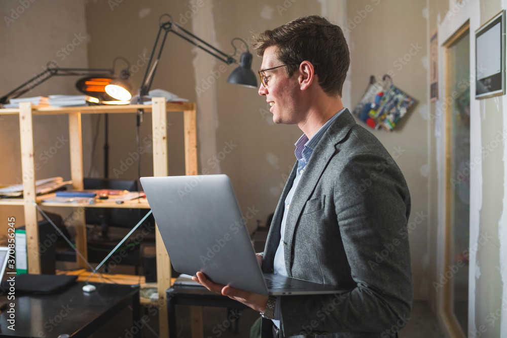 Smiling businessman holding laptop in office Smiling businessman holding laptop in office