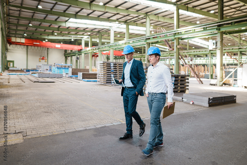 Two businessmen having a meeting and walking in a factory Two businessmen having a meeting and walking in a factory