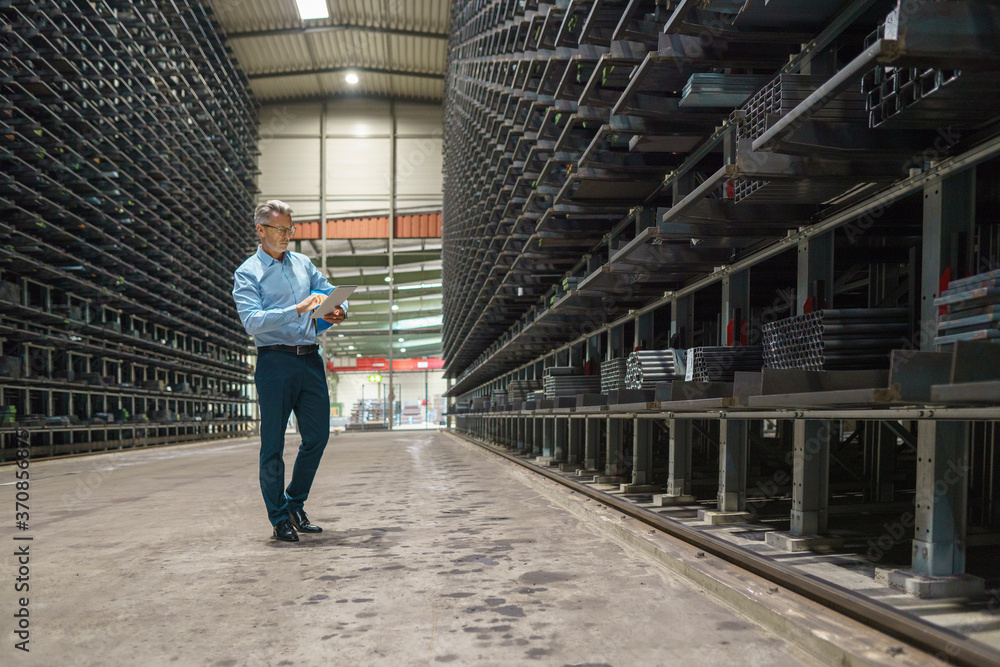 Mature businessman using tablet in a high rack warehouse of a factory Mature businessman using tablet in a high rack warehouse of a factory