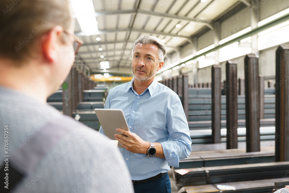 Businessman with tablet talking to employee in a factory Businessman with tablet talking to employee in a factory