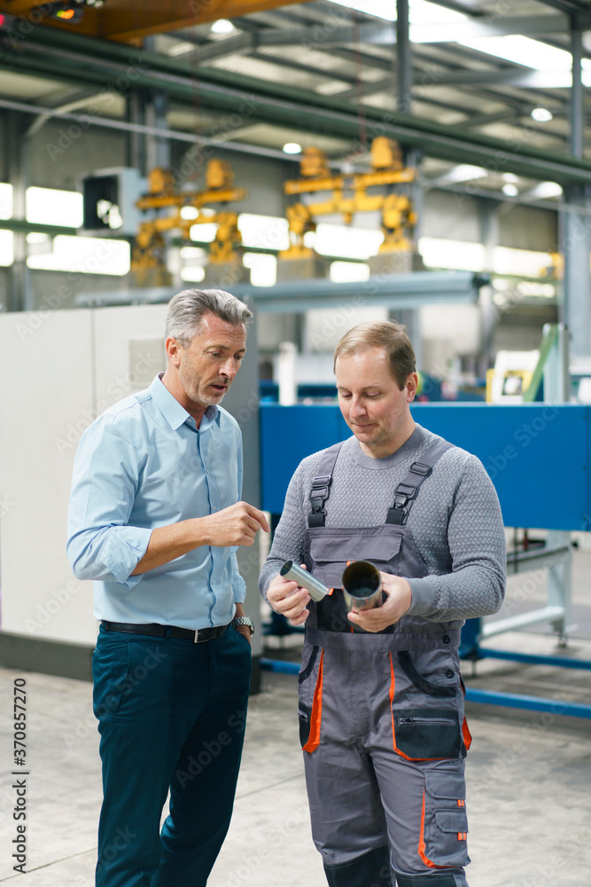 Businessman and worker examining steel pipe in a factory Businessman and worker examining steel pipe in a factory