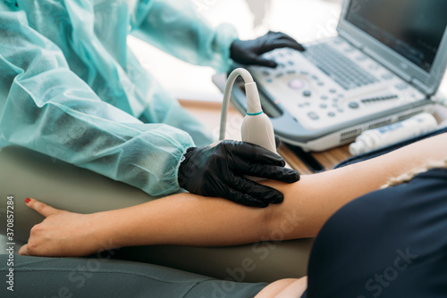 Doctor wearing protective clothes examining woman's arm with ultrasound scanner photo