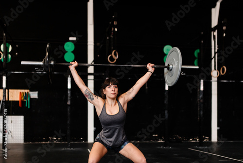 Female athlete lifting deadlift while standing in health club photo