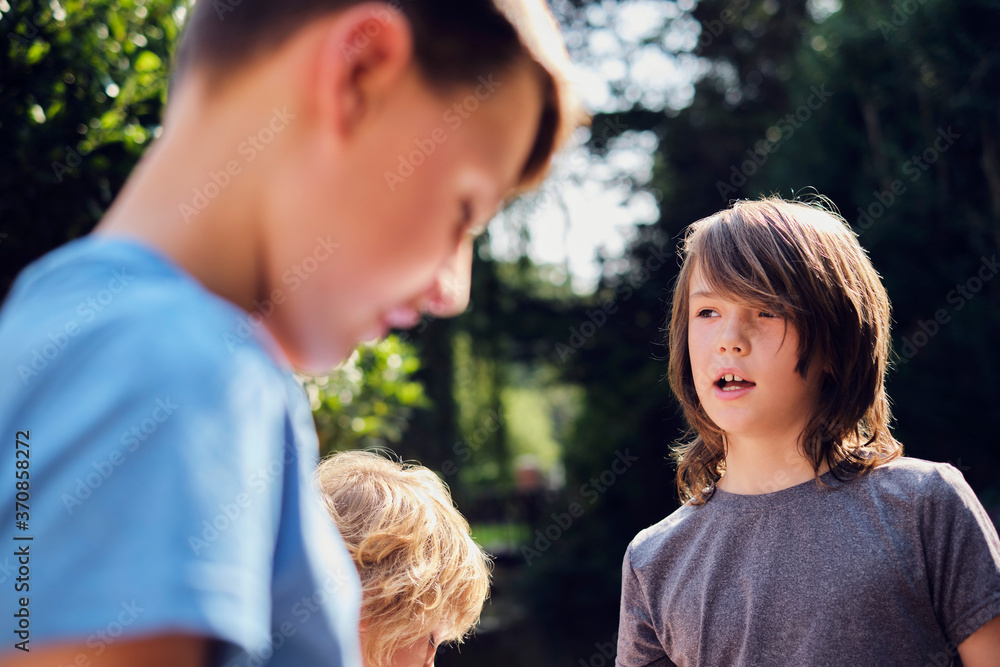 Boys talking while standing in forest during sunny day Boys talking while standing in forest during sunny day