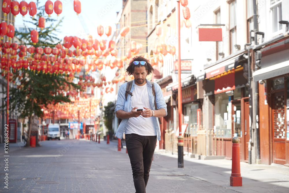 Young man walking on street looking at smartphone, Chinatown, London, UK Young man walking on street looking at smartphone, Chinatown, London, UK