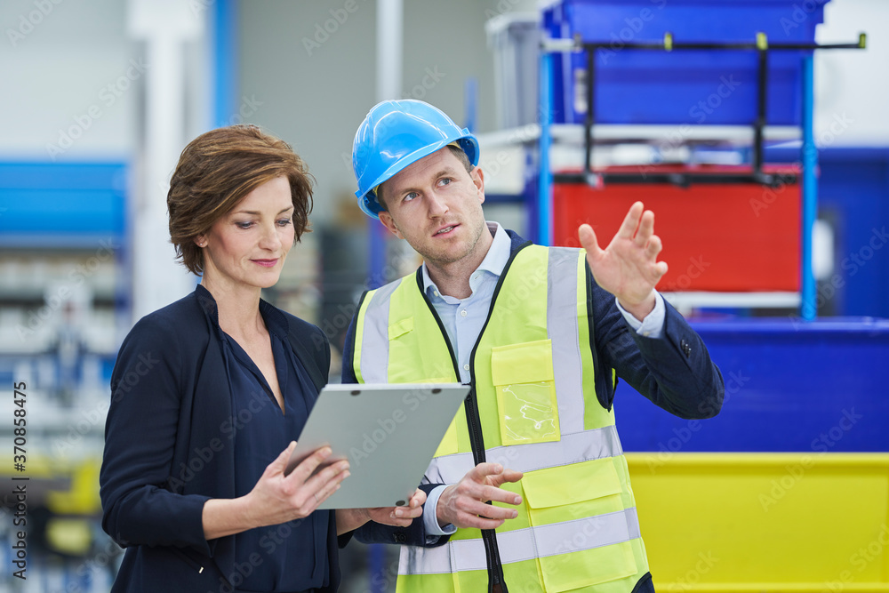 Supervisor explaining plan to female manager looking at clipboard in factory Supervisor explaining plan to female manager looking at clipboard in factory