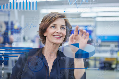 Happy female manager touching line graph on glass in industry photo