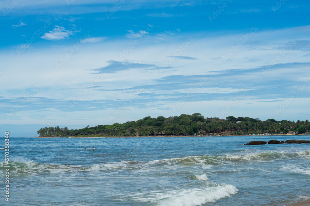 Surfer on the sea, palm trees on the background, blue sky. Arugam Bay, Sri Lanka. 