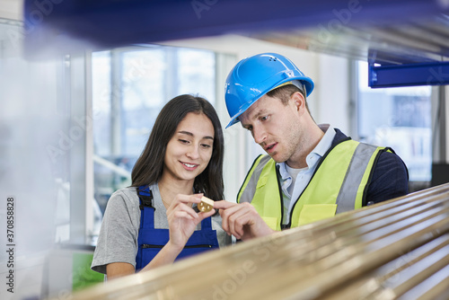 Female worker and supervisor examining metallic bolt in factory