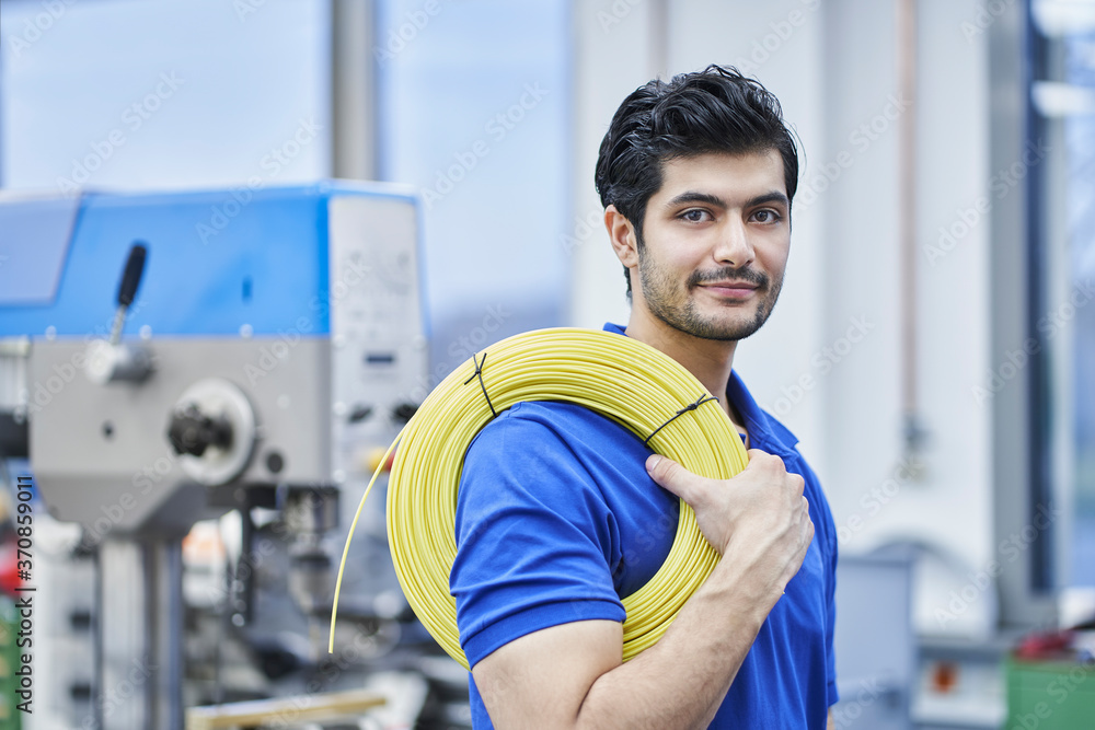 Confident male worker carrying rolled up cables in factory Confident male worker carrying rolled up cables in factory