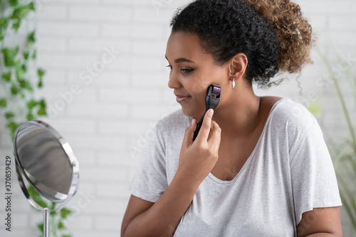 Young woman holding microneedler with dermaroller on face at home photo