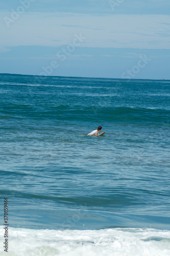 Surfer on the sea, palm turquoise water, blue sky. Arugam Bay, Sri Lanka. 