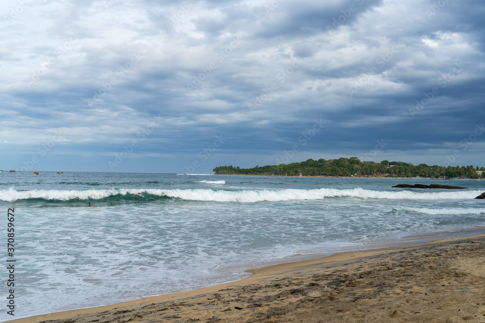 Tropical beach with waves and palm trees. cloudy sky. Arugam bay, Sri Lanka